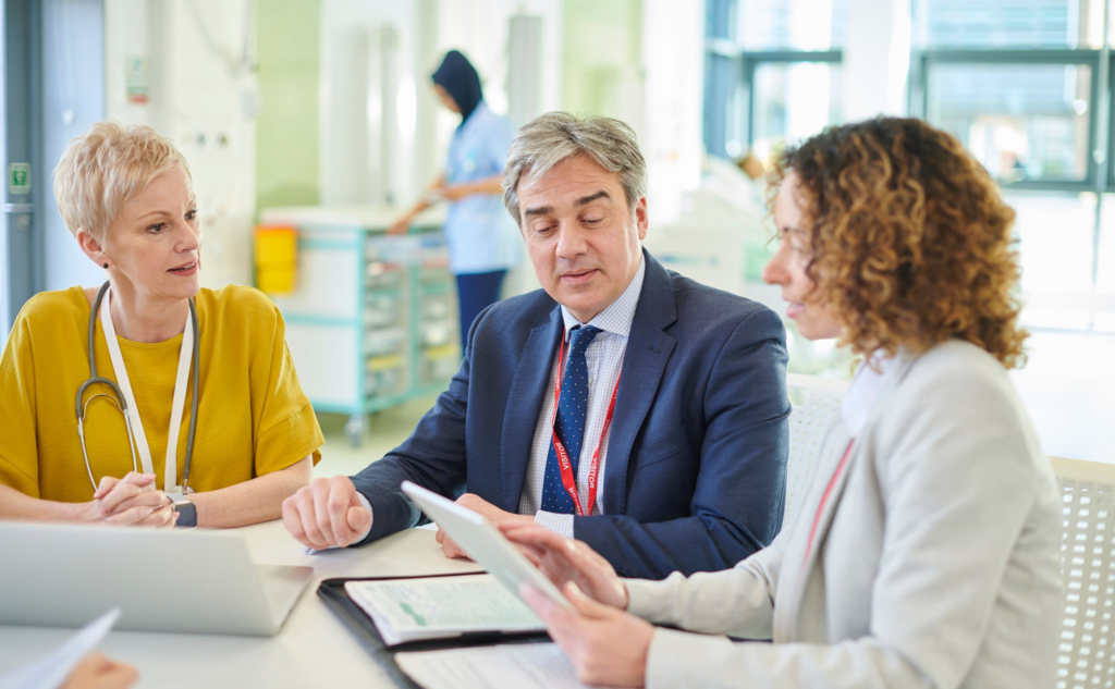 A doctor, a lawyer and a colleague reviewing case papers and a tablet together at a hospital table
